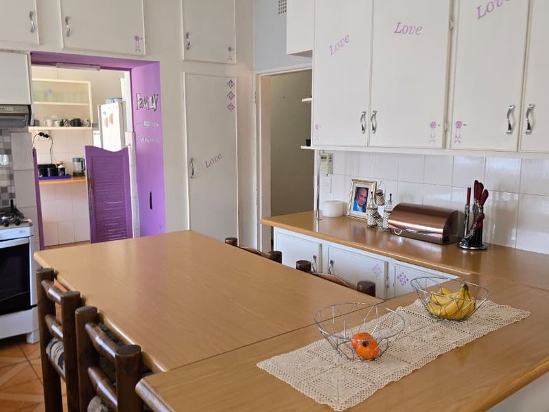 A dated kitchen featuring built-in cabinetry, laminate countertops, and a gas stove, with an adjacent scullery area visible through the doorway.