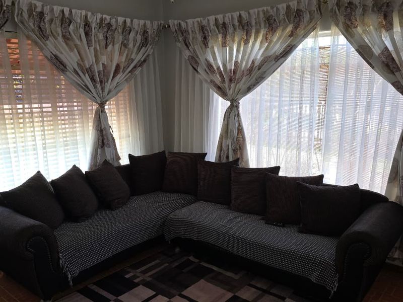 A cozy living room corner featuring large windows with decorative curtains and tiled flooring.