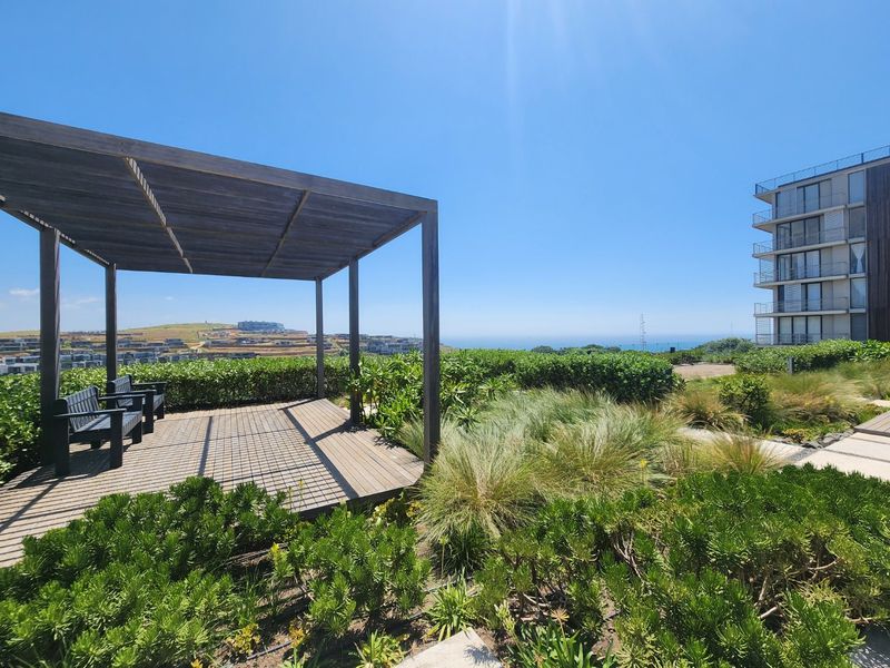 Outdoor timber pergola and decking area set within a landscaped garden, offering scenic coastal views.