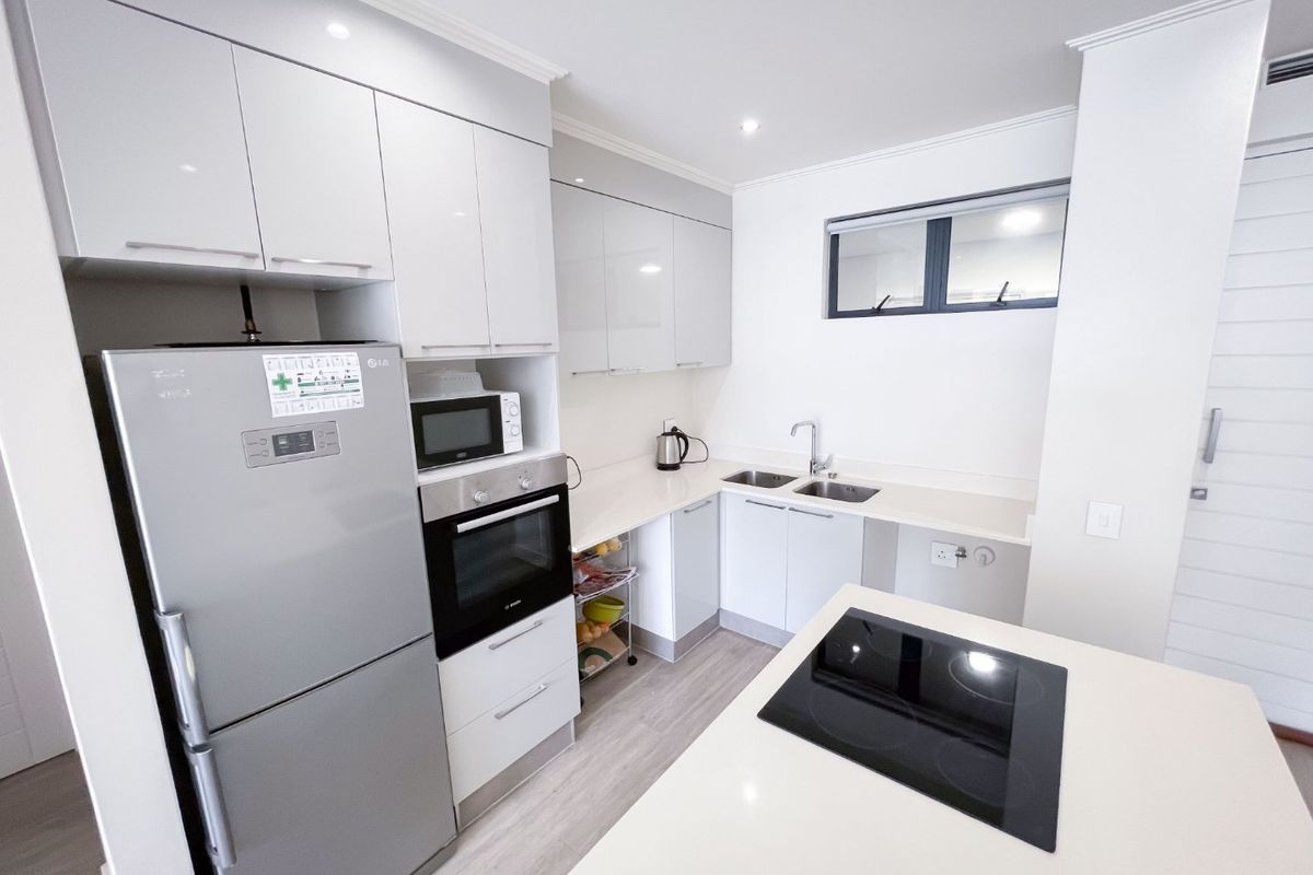 Modern kitchen featuring sleek white cabinetry, stone countertops, a central island with an integrated electric cooktop, and high-quality built-in appliances.
