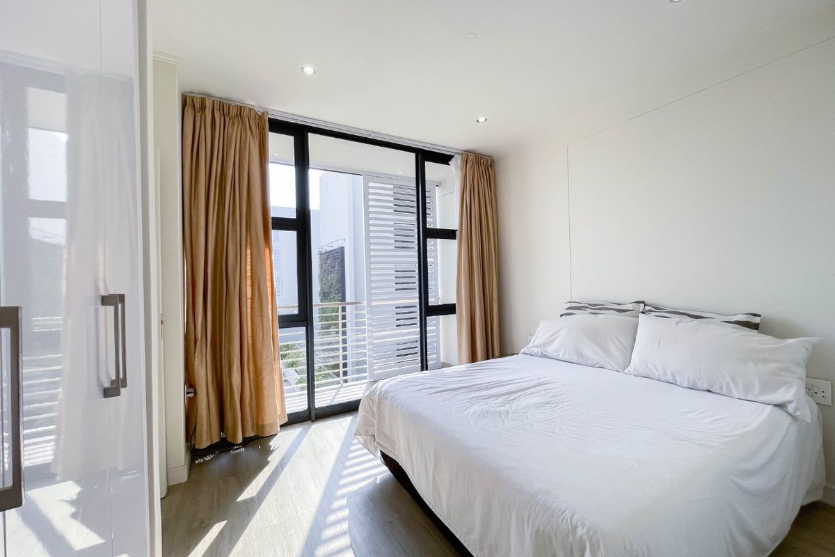 A bright, modern bedroom featuring laminate flooring, recessed lighting, and a large sliding glass door providing access to a private balcony.