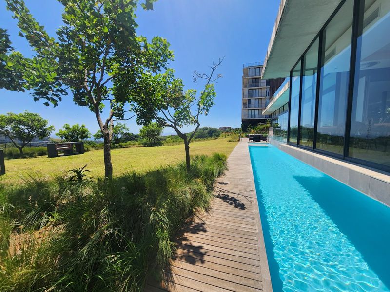 A modern lap pool featuring timber decking and expansive floor-to-ceiling glass windows, set within a beautifully landscaped garden area.