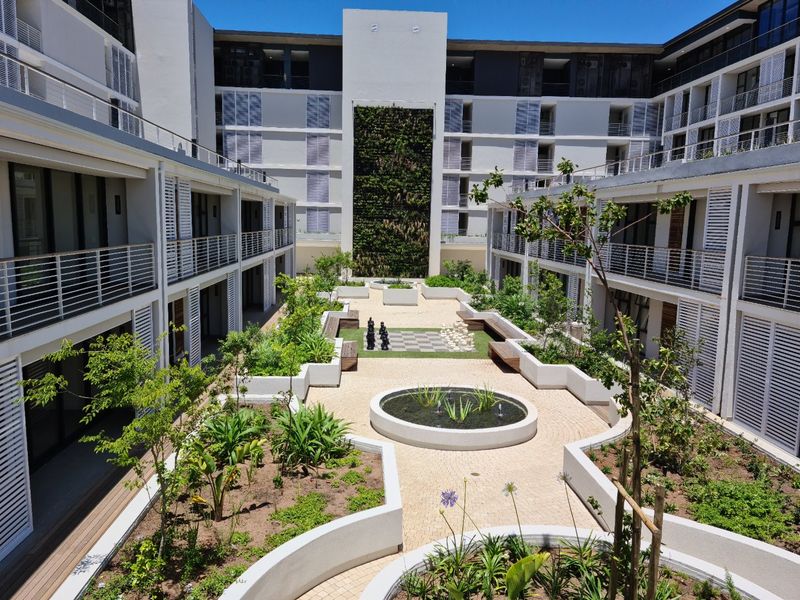 A well-maintained central courtyard featuring a vertical garden, water feature, paved walkways, and landscaped garden beds surrounded by apartment building wings.