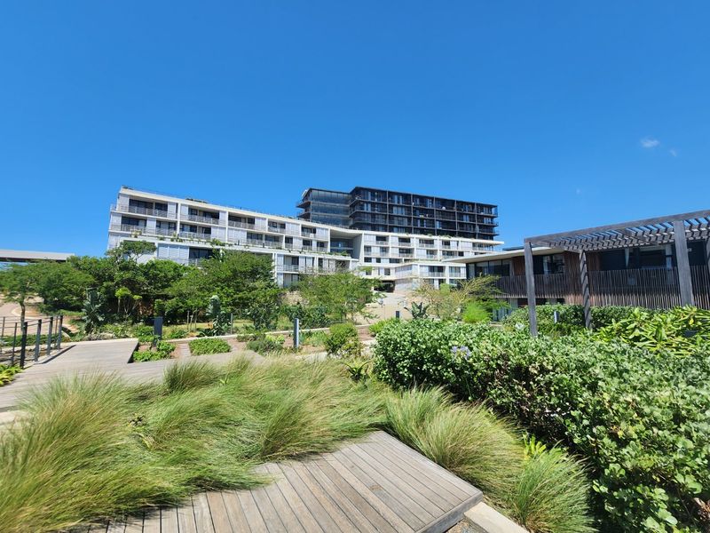 A view of the modern apartment complex exterior featuring landscaped gardens, timber decking, and a pergola area.