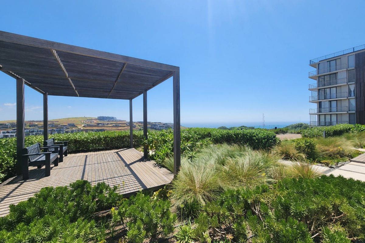 Outdoor timber pergola and decking area set within a landscaped garden, offering scenic coastal views.