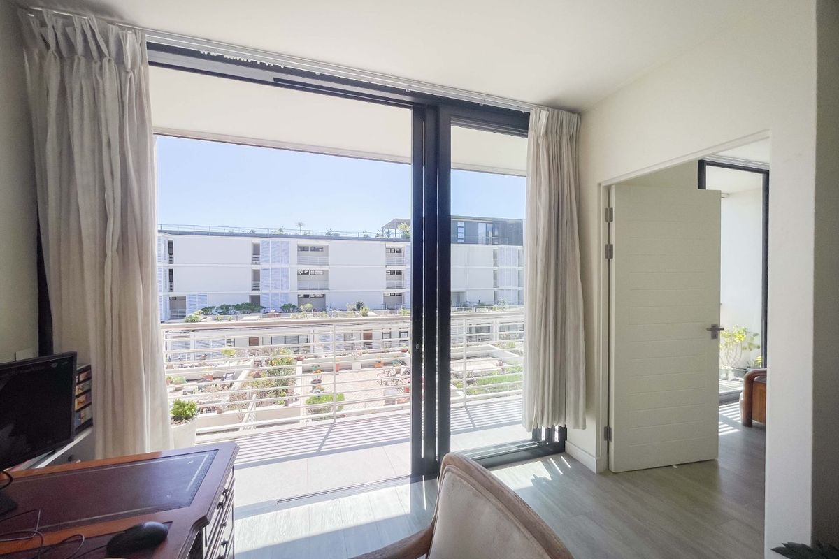 Bright bedroom featuring large sliding glass doors that open onto a private balcony, providing ample natural light and views of the surrounding complex.