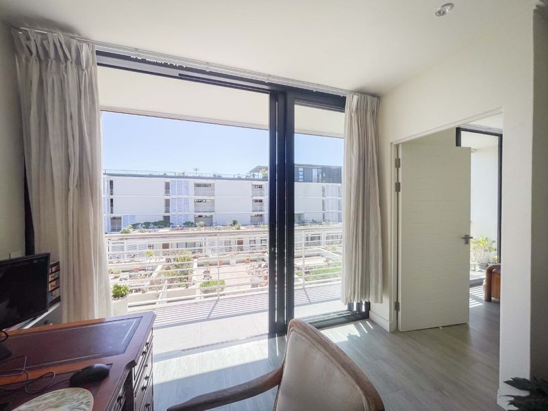 Bright bedroom featuring large sliding glass doors that open onto a private balcony, providing ample natural light and views of the surrounding complex.