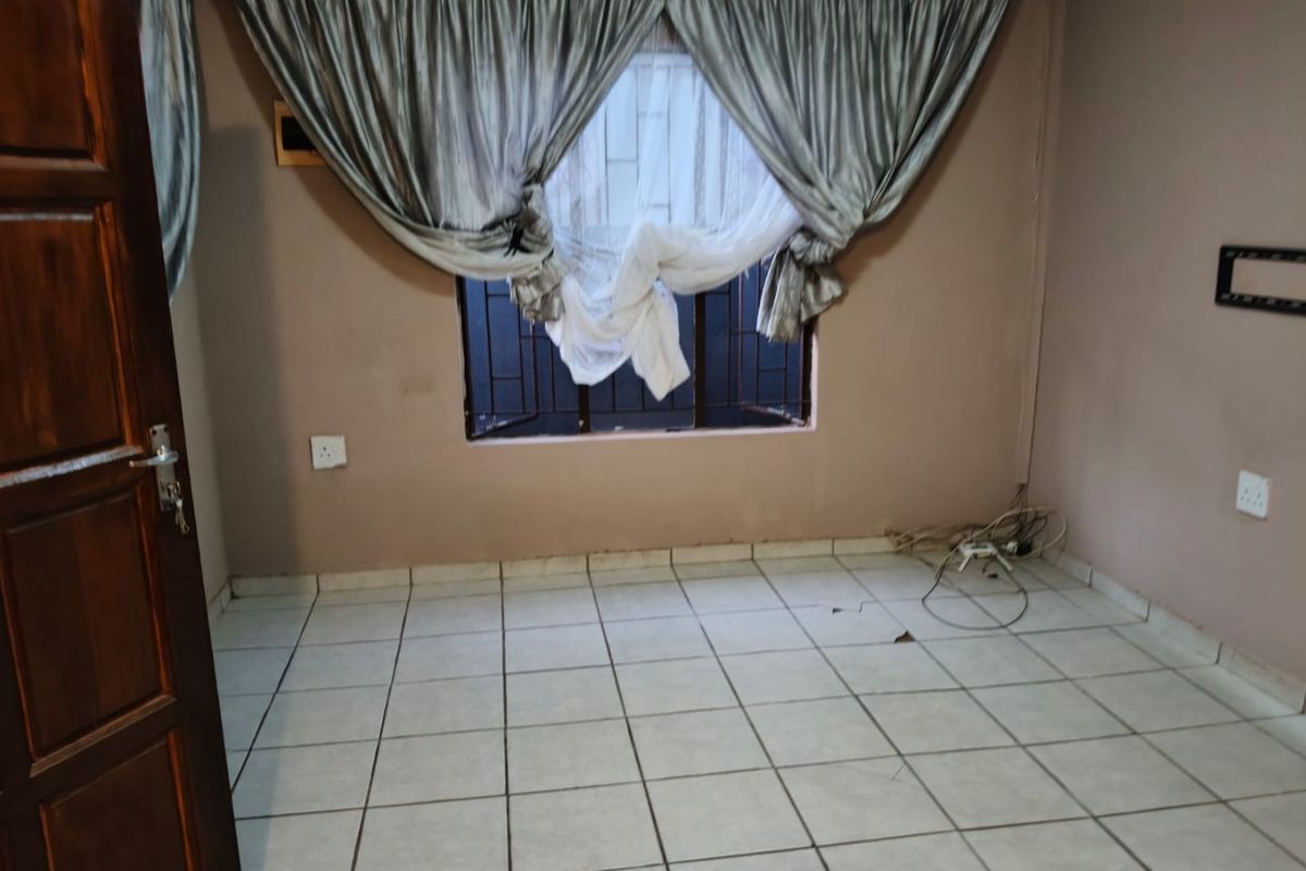 An empty bedroom featuring tiled flooring, a window with security bars, and a timber door. The space requires minor repairs and cosmetic updates.