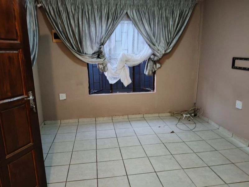 An empty bedroom featuring tiled flooring, a window with security bars, and a timber door. The space requires minor repairs and cosmetic updates.