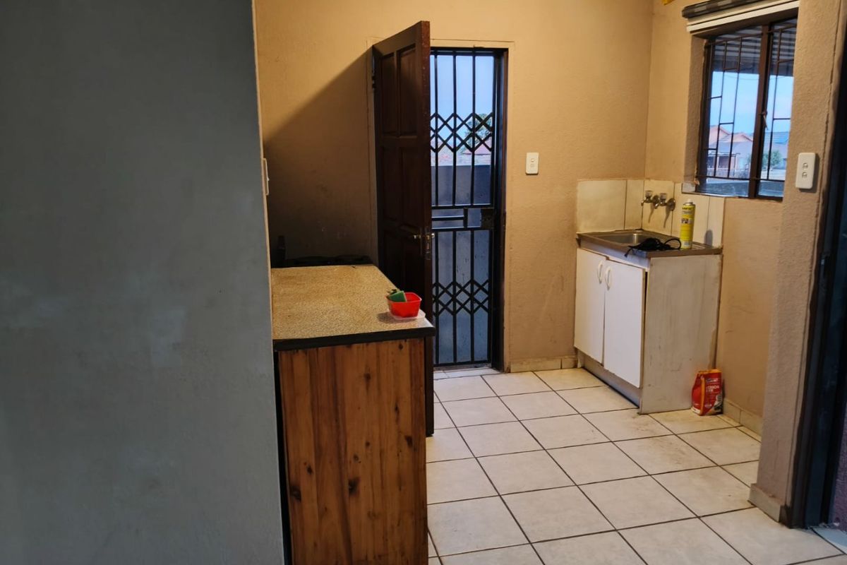 A functional scullery or utility area featuring tiled flooring, a single basin sink, and direct access to the exterior via a security gate.