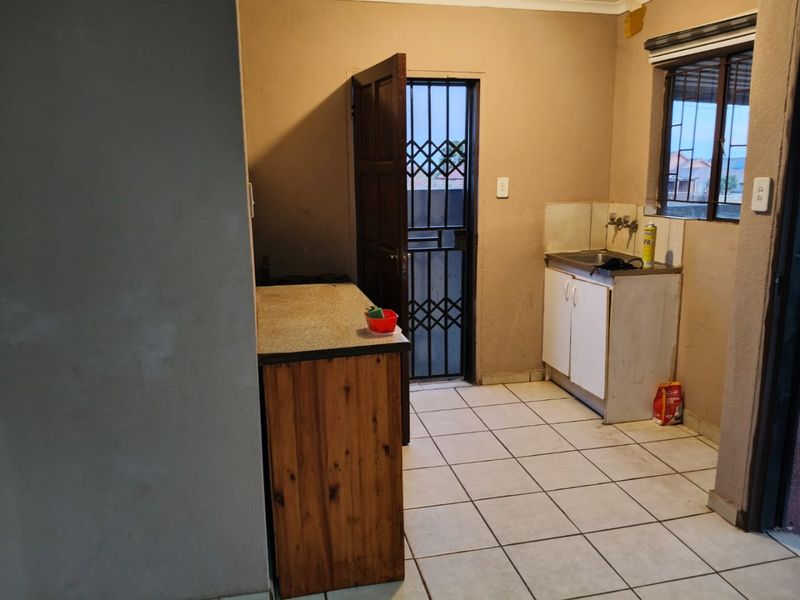 A functional scullery or utility area featuring tiled flooring, a single basin sink, and direct access to the exterior via a security gate.