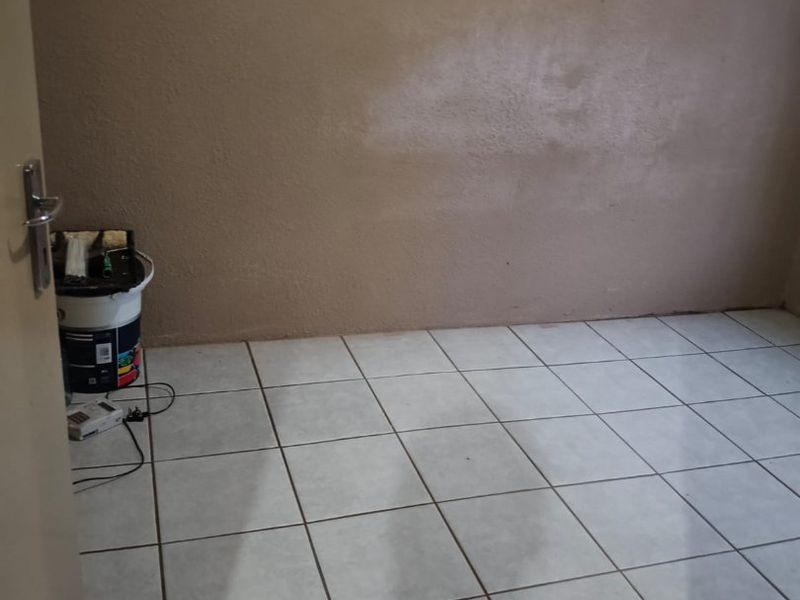 An empty bedroom featuring tiled flooring and walls requiring finishing or repainting.