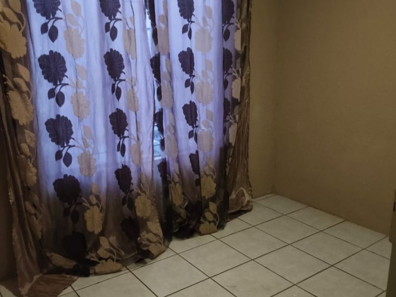 An empty bedroom featuring tiled flooring and a window with curtains.