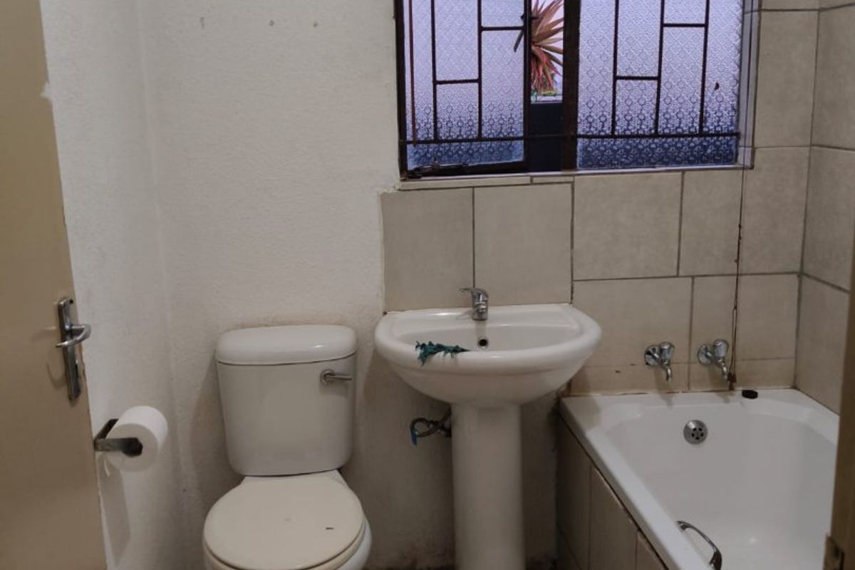 A functional bathroom featuring a pedestal basin, toilet, and bathtub with tiled finishes and security bars on the window.
