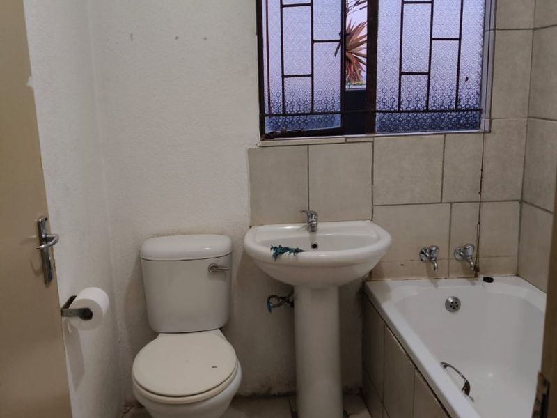 A functional bathroom featuring a pedestal basin, toilet, and bathtub with tiled finishes and security bars on the window.