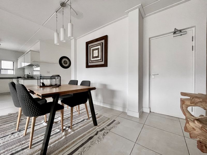 An open-plan living and dining area featuring neutral tiled flooring, modern pendant lighting, and a seamless transition into the adjacent kitchen space.