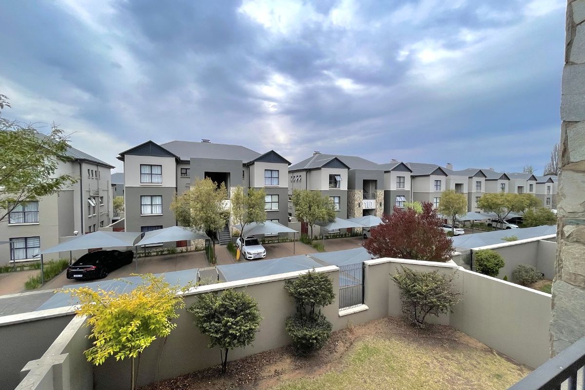 View of the apartment complex exterior featuring covered parking bays, landscaped garden areas, and secure boundary walls.