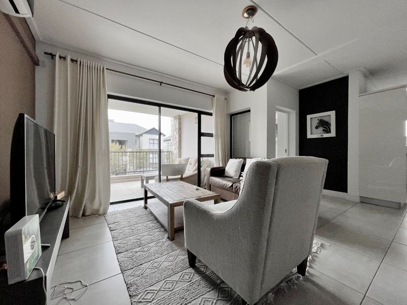 A bright living room featuring large sliding glass doors that open onto a balcony, tiled flooring, and a modern ceiling light fixture.