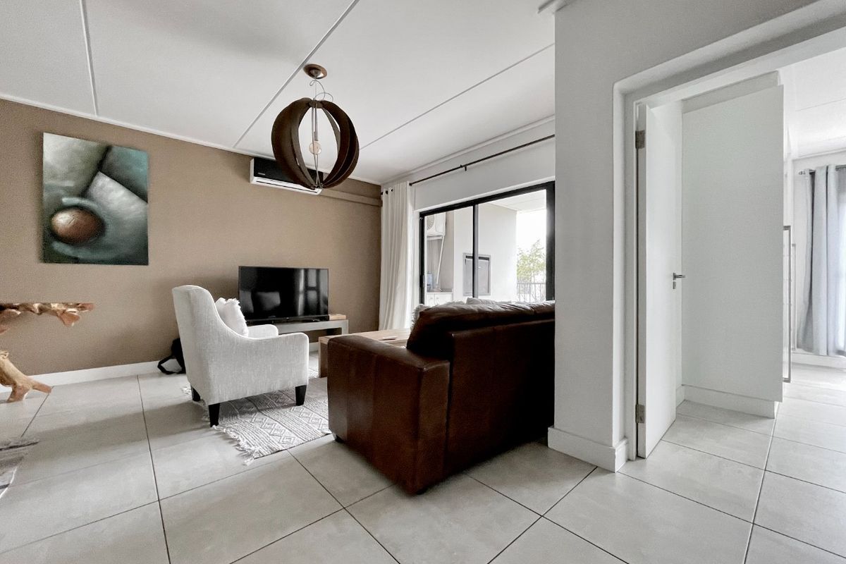 A bright and well-maintained living room featuring neutral tiled flooring, a wall-mounted air conditioning unit, and sliding glass doors leading to an outdoor area.