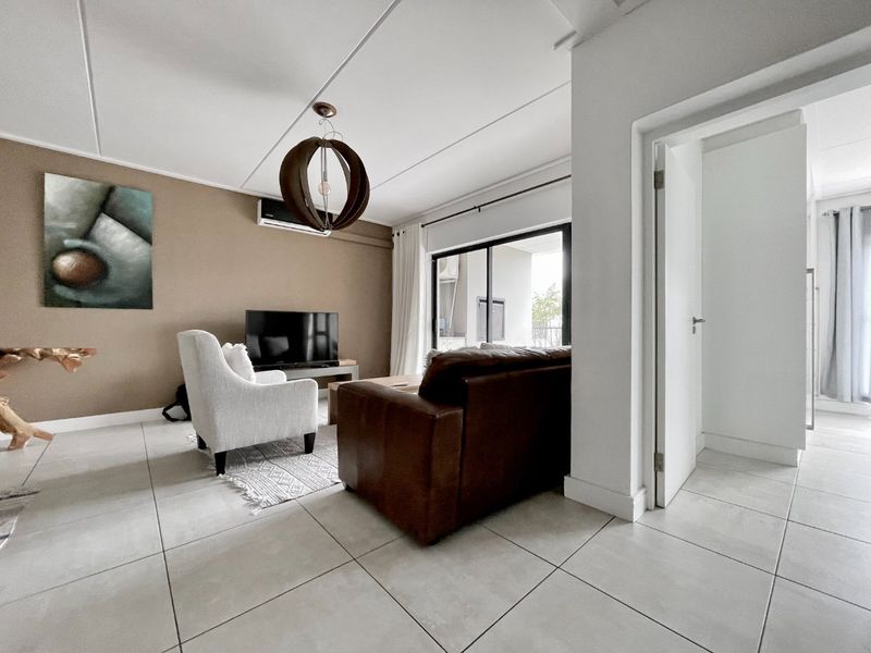 A bright and well-maintained living room featuring neutral tiled flooring, a wall-mounted air conditioning unit, and sliding glass doors leading to an outdoor area.