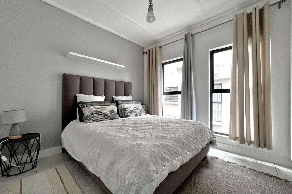 A well-maintained bedroom featuring tiled flooring, neutral wall tones, and large windows with fitted curtain rods, providing ample natural light.