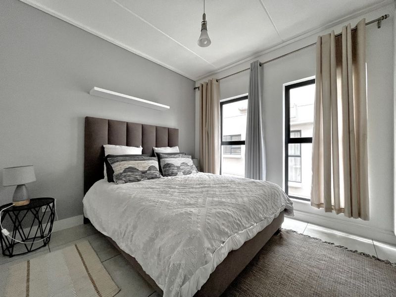 A well-maintained bedroom featuring tiled flooring, neutral wall tones, and large windows with fitted curtain rods, providing ample natural light.