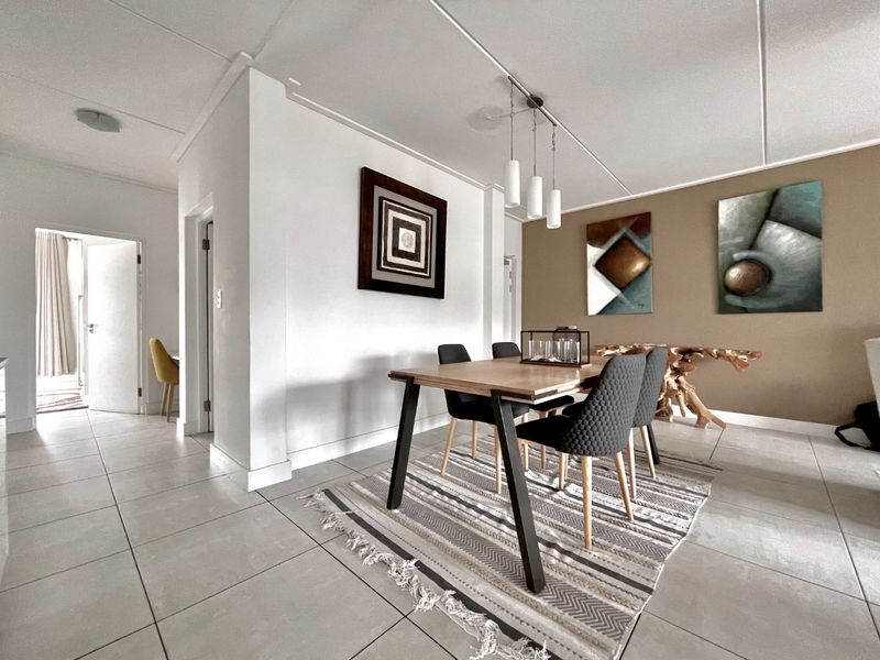 A bright and well-maintained dining area featuring neutral tiled flooring, modern pendant lighting, and a clean, contemporary aesthetic.