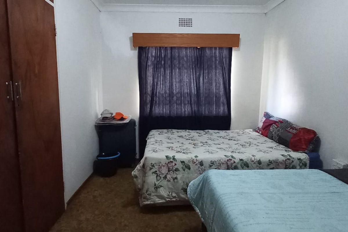 A bedroom featuring a built-in wooden wardrobe, carpeted flooring, and a window with a wooden pelmet.