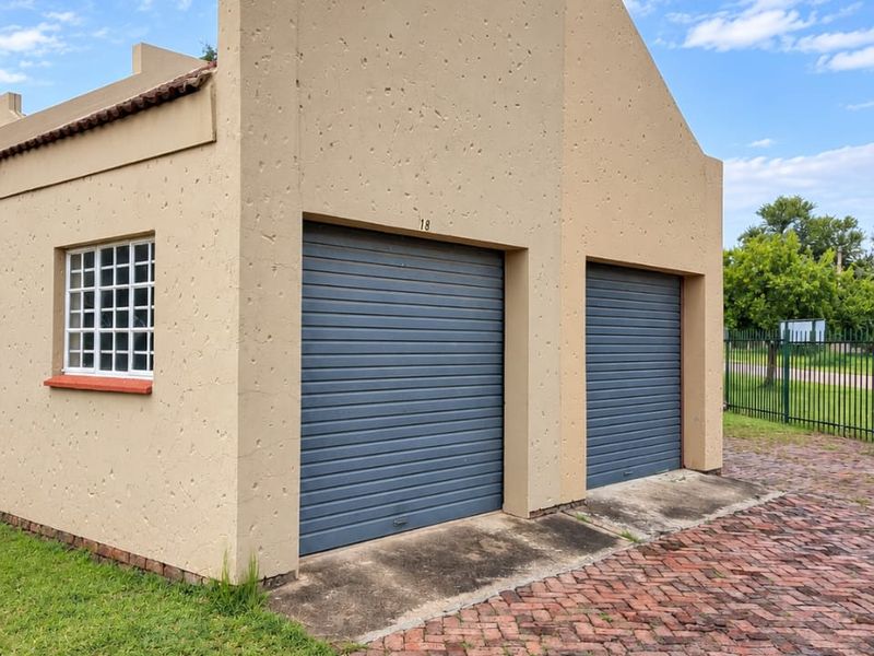 A detached double garage featuring textured exterior walls, two roller doors, and a brick-paved driveway in a residential setting.