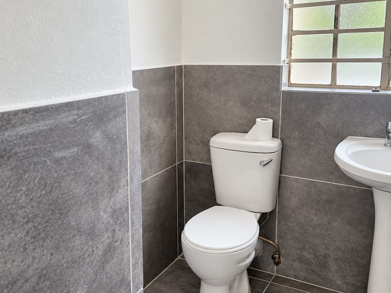 A clean and modern bathroom featuring grey floor-to-ceiling tiles, a white pedestal basin, and a standard toilet.