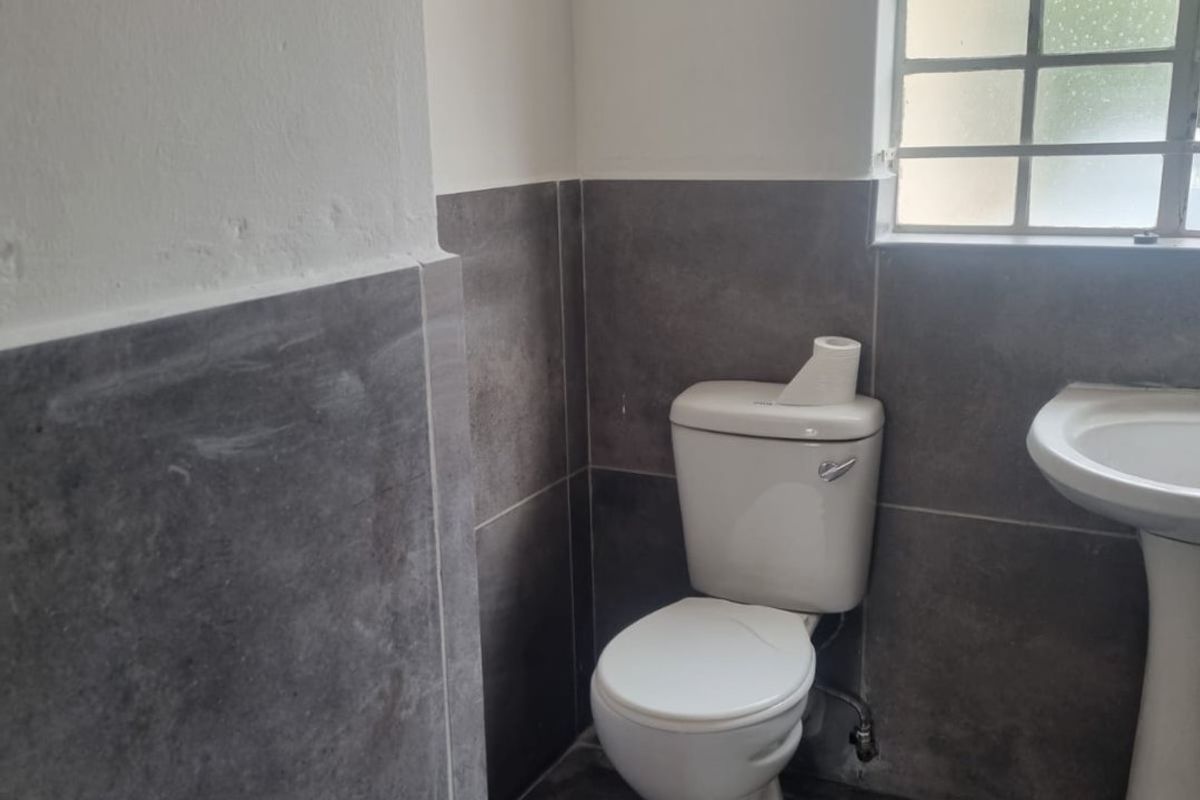 A compact bathroom featuring a pedestal basin, toilet, and modern grey floor-to-wall tiling with a window providing natural light.