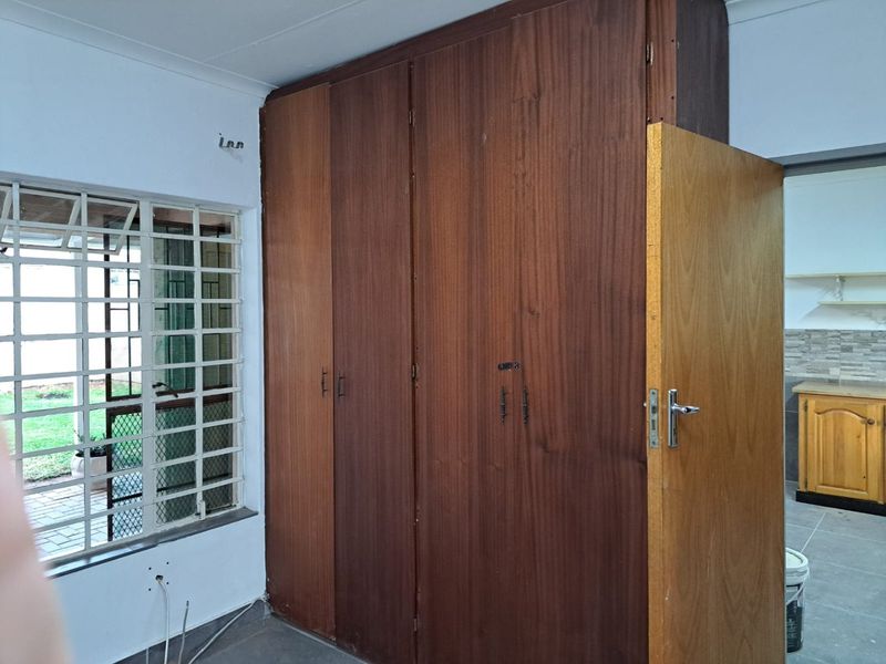 A bedroom featuring built-in wooden cupboards, security bars on the window, and direct access to an adjacent kitchen area.