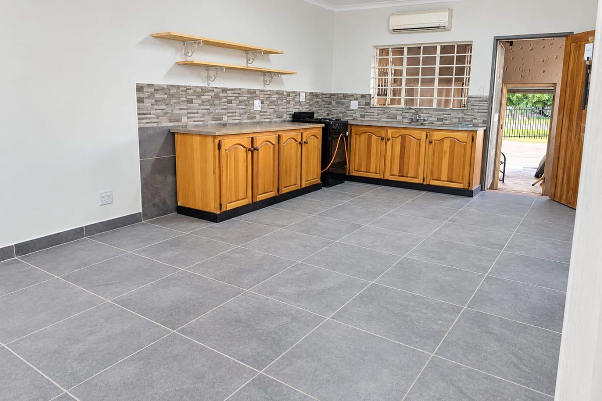 A clean, functional kitchen featuring wooden cabinetry, tiled flooring, a tiled splashback, and a wall-mounted air conditioning unit, offering a bright and open layout.