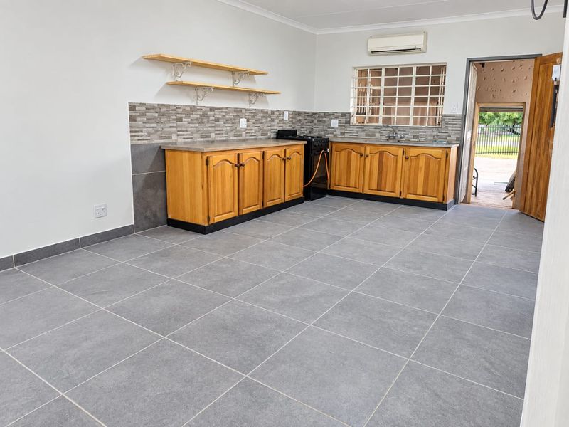 A clean, functional kitchen featuring wooden cabinetry, tiled flooring, a tiled splashback, and a wall-mounted air conditioning unit, offering a bright and open layout.
