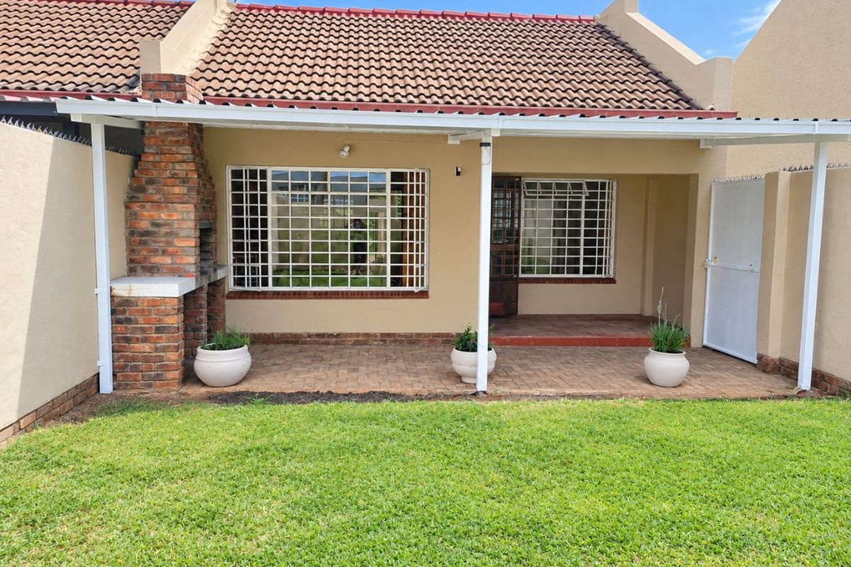 Rear exterior view of the townhouse featuring a covered patio with a built-in brick braai, security bars on windows, and a private garden area.