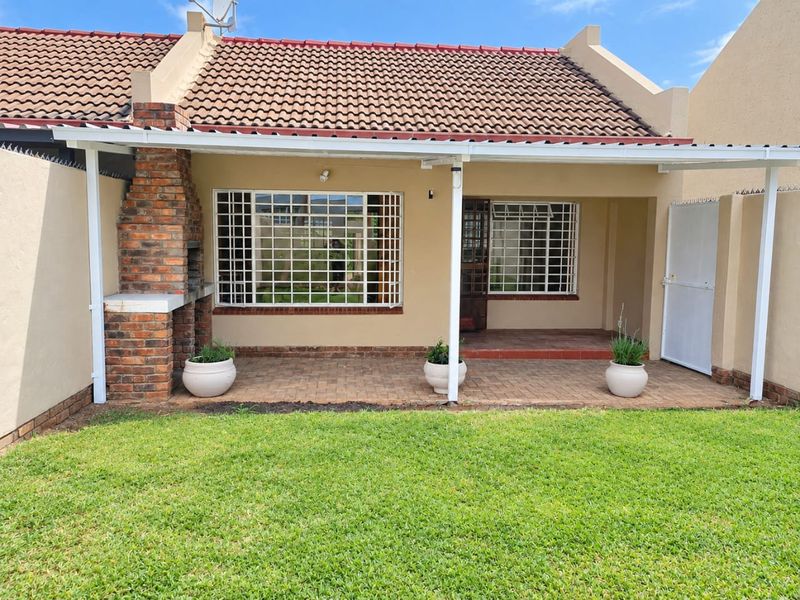 Rear exterior view of the townhouse featuring a covered patio with a built-in brick braai, security bars on windows, and a private garden area.