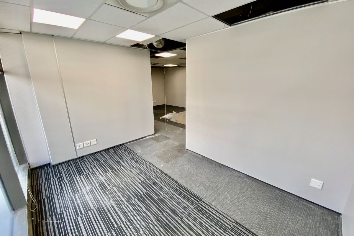 An empty commercial office space featuring suspended ceilings with missing tiles, carpeted flooring, and recessed lighting, currently requiring maintenance and finishing.