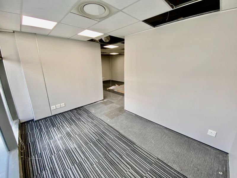 An empty commercial office space featuring suspended ceilings with missing tiles, carpeted flooring, and recessed lighting, currently requiring maintenance and finishing.