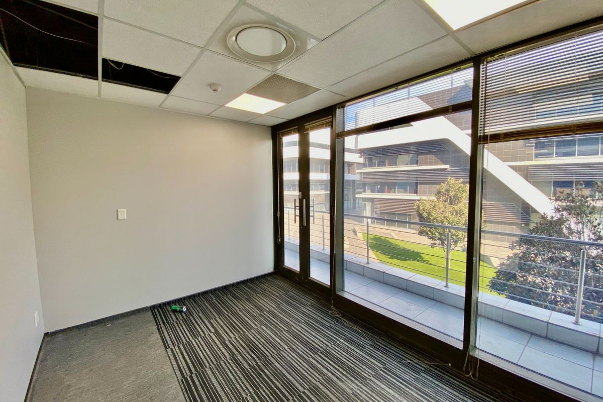 Empty office space featuring a suspended ceiling, floor-to-ceiling windows, and direct access to a private balcony with modern building views.