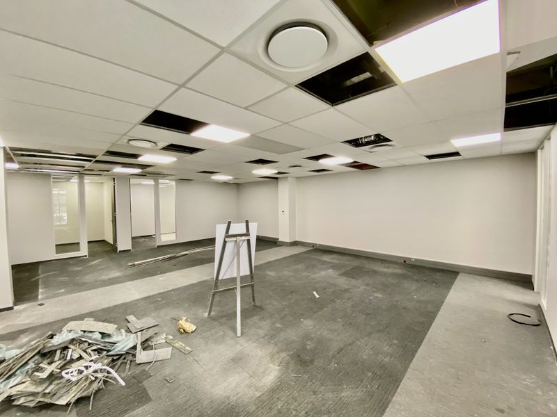 Vacant commercial office space featuring a suspended ceiling with missing tiles, glass partitions, and carpet flooring, currently undergoing maintenance or renovation.