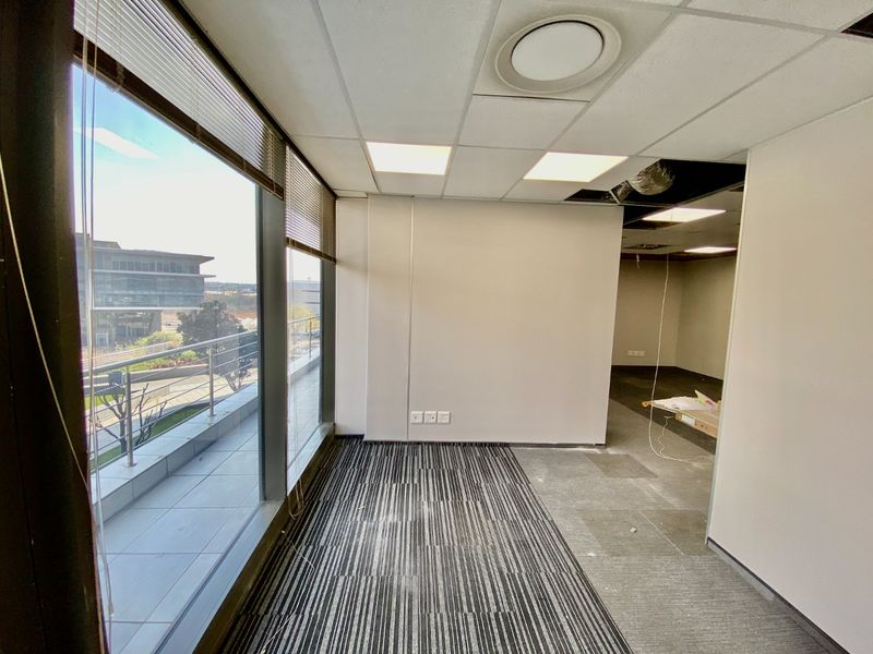 Empty commercial office space featuring large windows with balcony access, carpeted flooring, and a suspended ceiling requiring minor repairs.