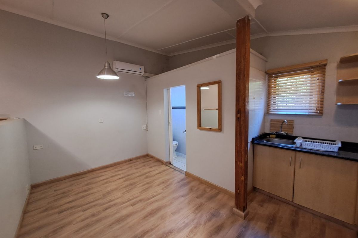 Open-plan living area featuring laminate flooring, a compact kitchen with granite countertops, and a split-system air conditioner, leading to an adjacent bathroom.