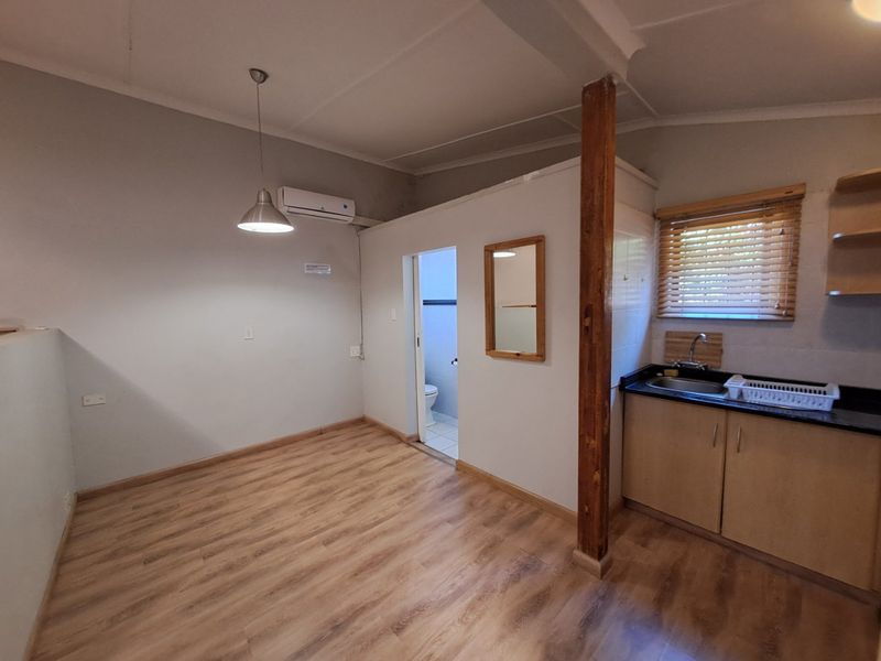 Open-plan living area featuring laminate flooring, a compact kitchen with granite countertops, and a split-system air conditioner, leading to an adjacent bathroom.