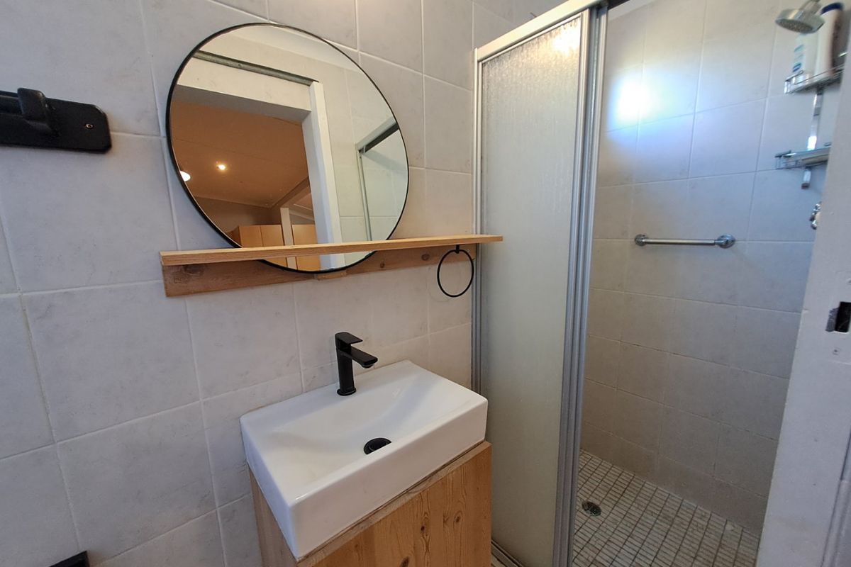 A functional bathroom featuring a modern vessel sink with a black mixer tap, a wooden vanity, and a glass-enclosed shower with tiled finishes.