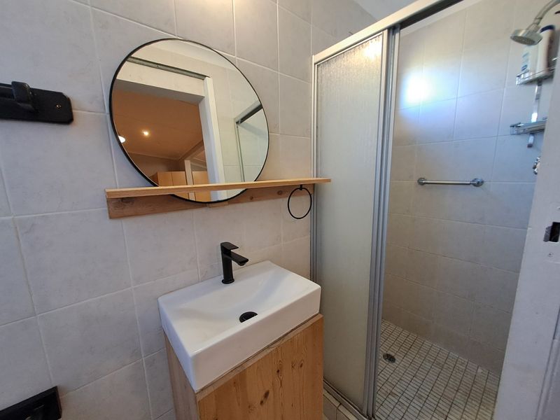 A functional bathroom featuring a modern vessel sink with a black mixer tap, a wooden vanity, and a glass-enclosed shower with tiled finishes.