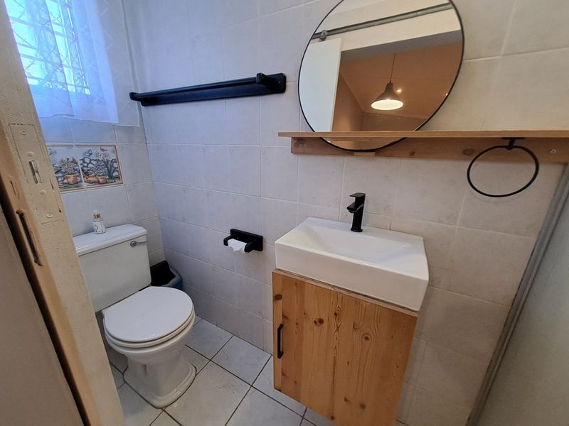A compact bathroom featuring a wall-mounted wooden vanity with a modern basin, black fixtures, and neutral wall and floor tiling.