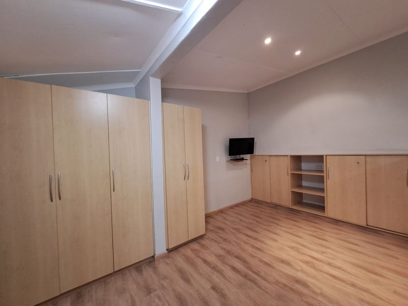 Spacious bedroom featuring extensive built-in cabinetry, light wood-look laminate flooring, and modern recessed ceiling lighting.