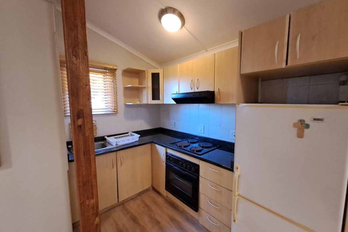 A functional kitchen featuring light wood cabinetry, dark granite countertops, built-in oven, electric hob, and a tiled splashback.