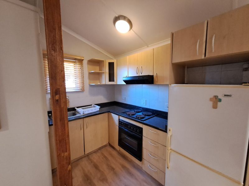 A functional kitchen featuring light wood cabinetry, dark granite countertops, built-in oven, electric hob, and a tiled splashback.