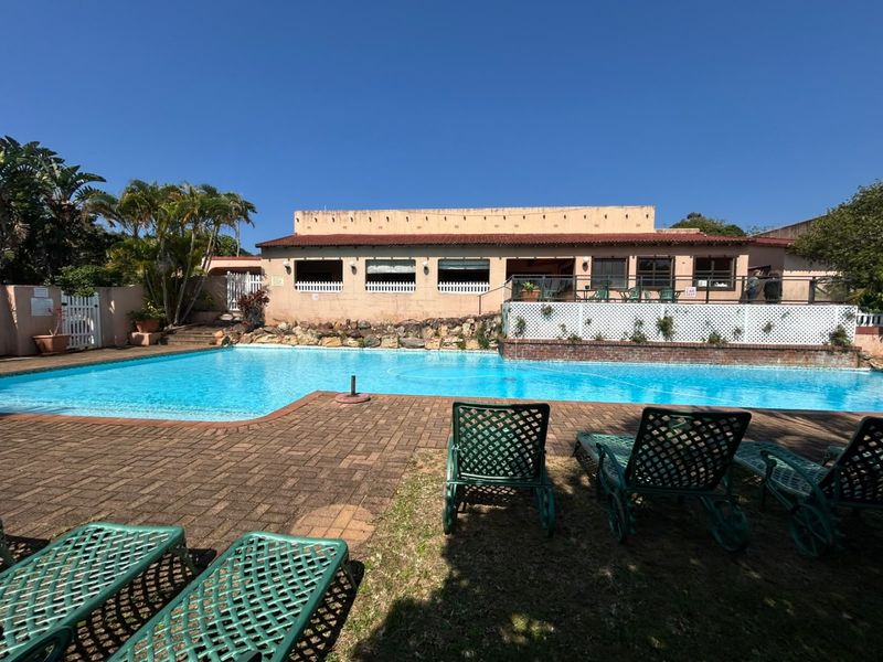 A spacious outdoor pool area featuring brick paving, a large swimming pool, and a rear building elevation with a tiled roof.
